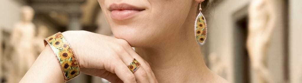 Banner for art jewelry collections featuring a model wearing colorful, handmade copper jewelry sets in a warm setting.