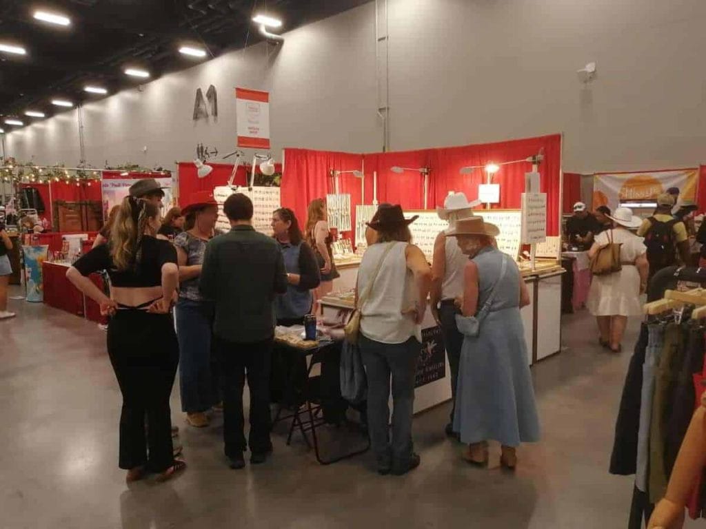The Copper Reflections booth at a local craft show, displaying a beautiful collection of handmade copper art jewelry, including vibrant earrings, bracelets, and rings with sparkling finishes.